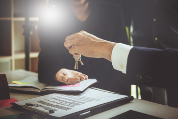 Agents are giving house keys of customer and contract paper on desk at agency office. Agreement...