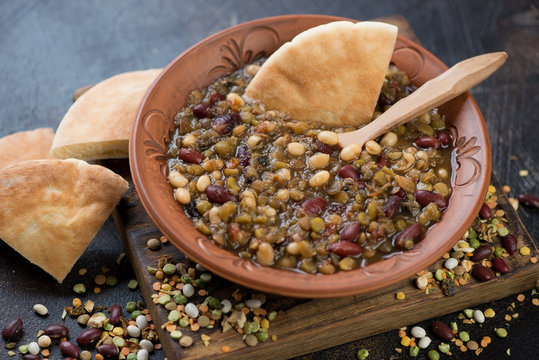 Thick soup with variety of beans served in a clay plate with pita, studio shot