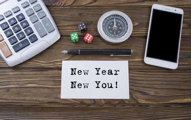 New Year New You written on paper, wooden background desk with calculator, dice, compass, smart phone and pen.Top view conceptual.