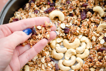 Female hand holds granola against the background of baking sheet with granola. Close-up