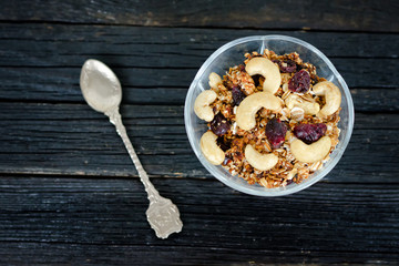 Granola with cashew in a bowl, a teaspoon. Black wooden table