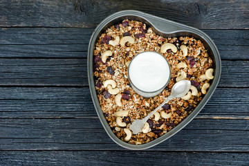 Glass of yogurt and granola with cashews in a pan. Black wooden table