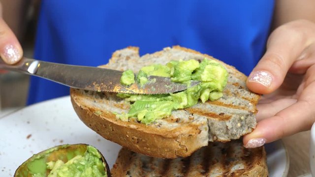 Female Hands Spreading Avocado On Healthy Whole Grain Bread For Breakfast. Closeup. 4K. 