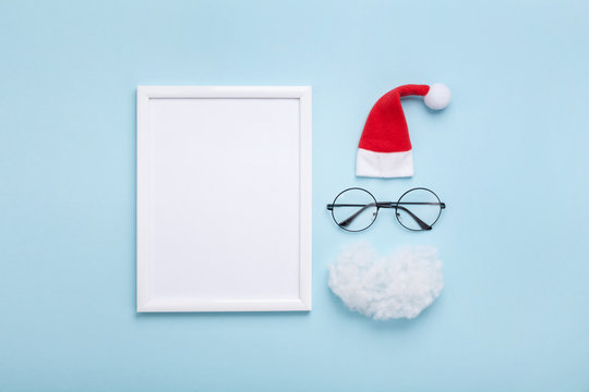 Picture frame, santa hat, beard and glasses on blue background top view. Creative christmas mockup. Greeting card, invitation or flyer. Flat lay.