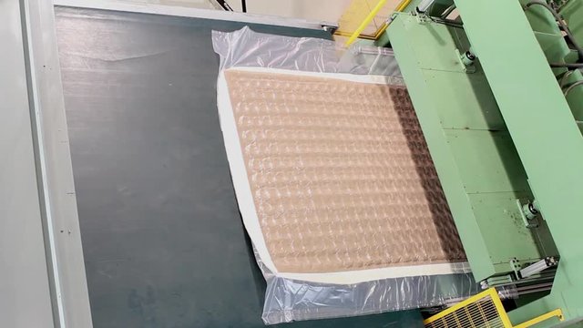 The mattress unit is supplied under a hydraulic press and compressed, hydraulic press compresses and wraps the mattress in cellophane, factory mattresses