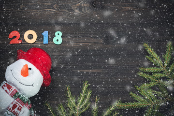Happy New Year 2018 of real wooden figures with snowman and fir tree branches with snow on dark wooden background