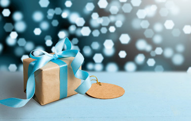 Christmas gift or New Year with blue ribbon and greeting card on wood table on bokeh background. Tiny and Handmade gift box concept.