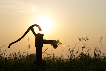 The silhouette water pump on the grass and rice field with the sun on the evening , with copy space