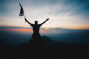 Young man holding flag to conquer the mountain. Silhouette style.