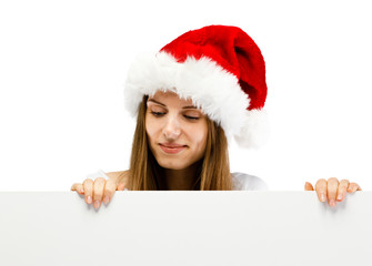 Beautiful woman in Santa Claus clothes peeking behind blank board on white background