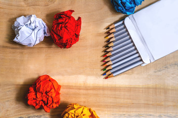 colored pencils in a box on a wooden table with colored paper
