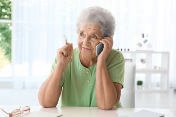 Elderly woman speaking on cell phone at home