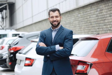 Young car salesman in formal suit near parked automobiles outdoors