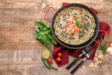 Frying pan with delicious spinach frittata on wooden background