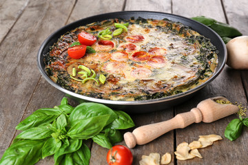 Frying pan with delicious spinach frittata on wooden background