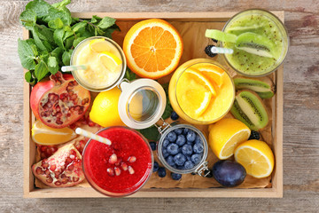 Glasses with different smoothies and fruits in wooden box on table