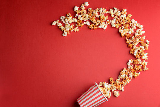 Overturned cup with tasty caramel popcorn on color background
