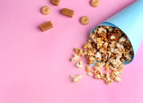 Paper cone with tasty caramel popcorn on color background