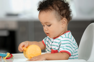 Cute baby with bottle of water sitting in kitchen