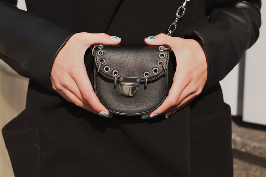 Woman's hands holding small fashionable handbag at the background of street
