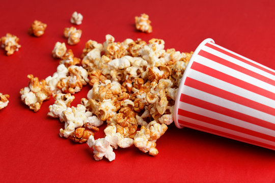 Paper cup with caramel popcorn on color background