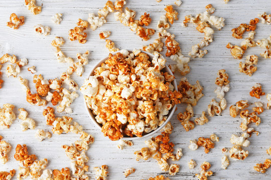 Bowl with caramel popcorn on white wooden background