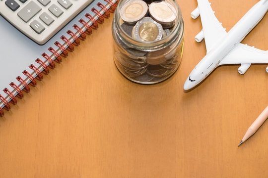 Travel and planning concept. Airplane toy model with full of coins in bottle, calculator, pencil and notebook, on wooden table.
