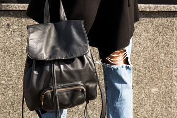 Closeup shot of  black leather backpack at the woman's legs