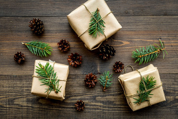 Gifts for new year wrapped in craft paper near spruce branches and cones on wooden background top view pattern