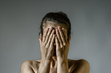 Concept of fear, shame, domestic violence. Woman covers her face her hands on scratched background.