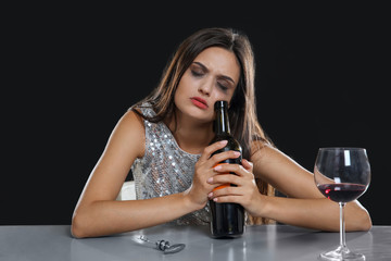 Young woman drinking alcohol at table against black background