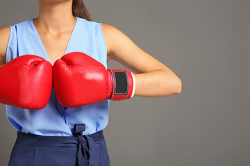 Businesswoman in boxing gloves on grey background