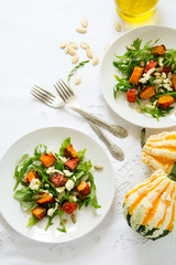 Fresh autumn salad with baked pumkin, arugula, cheese and seeds on white table cloth. Space for copy