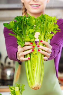 Woman in kitchen holds green celery