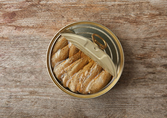 Open tin can with fish on wooden background