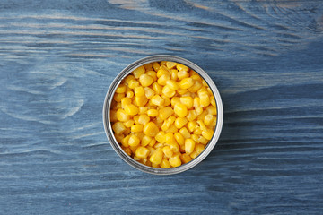 Open tin can with corn kernels on wooden background