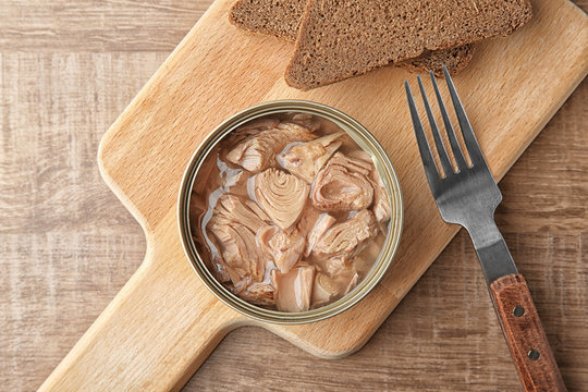 Open tin can with fish and bread on wooden background