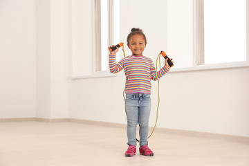 Cute African American girl skipping rope in light room