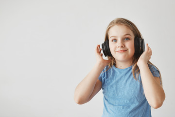 Naklejka premium Funny cheerful girl with light hair and blue eyes, wearing headphones. looking in camera with shocked expression after loud music suddenly starts to play