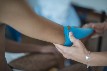 fisioterapista applica tape dopo massaggio per il dolore a un giovane sportivo

