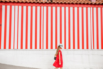 Young woman in red dress on the striped wall background. Wide geometrical view with copy space