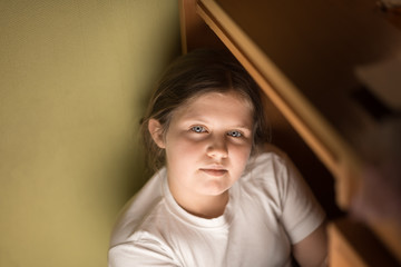 Fototapeta premium Small girl hiding under a table and plays games on the phone. To hide from problems. Concept.