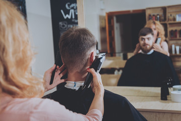 Master cuts hair and beard of men, hairdresser makes hairstyle for a young man. Hipsters
