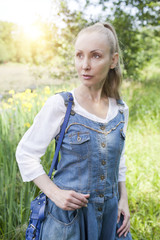 the beautiful slender young woman in a blue sundress and a white blouse on the bank of the forest lake in sunny day..