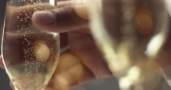 Close up of a man's hand picking up a flute glass with sparkling wine with bubbles in gray and gold tones