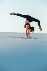 Young woman practicing inversion balancing yoga pose handstand on sand.