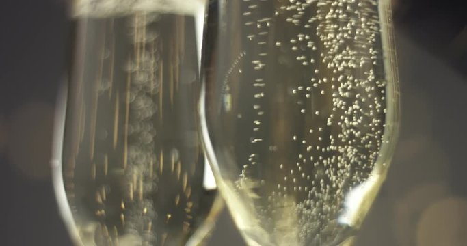 Close up video of trails of bubbles going up in champagne glasses on gray background with blurred lights in warm tones