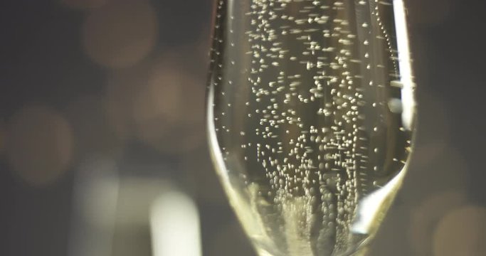 Close up video of trails of bubbles going up in champagne glasses on gray background with blurred lights in warm tones