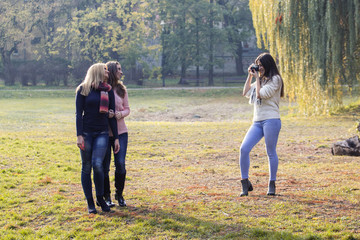 Three girls havin fun in park, one of them have old film camera and taking pictures of two young long hair girls who posing