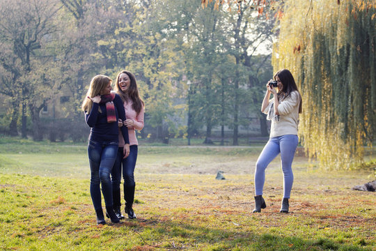 Three girls havin fun in park, one of them have old film camera and taking pictures of two young long hair girls who posing